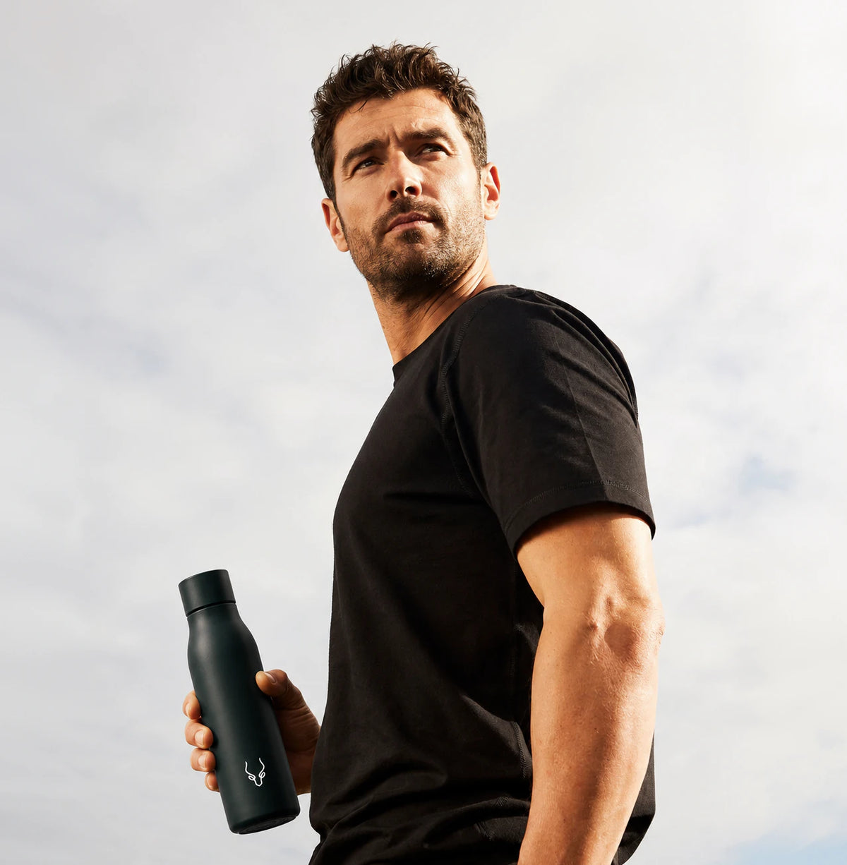 Athlete in a black T-shirt holding a Yakuru water bottle against the sky